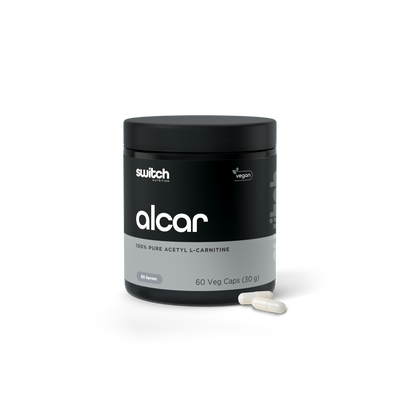 A container of 'alcar 100% pure acetyl L-carnitine' by Switch Nutrition, labeled as vegan, with 60 vegetable capsules (30 grams) and two visible capsules in front of the container.