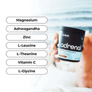 A hand holding a black jar labeled 'adrenal' with a list of ingredients such as Magnesium, Ashwagandha, Zinc, L-Leucine, L-Theanine, Vitamin C, and L-Glycine, on a blurred white background.