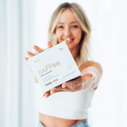 A smiling woman in a white top, presenting a product box labeled 'coffee switch' towards the camera, in a softly lit and blurred background.