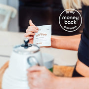 A person holding a sachet of 'coffee switch' next to a stainless steel kettle, with a blurry kitchen setting in the background and a '30 day money back guarantee' badge in the upper corner.