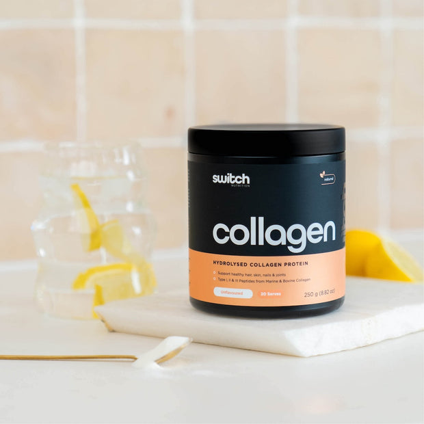 Black collagen switch tub from switch nutrition on a bench with a glass of liquid in the background.