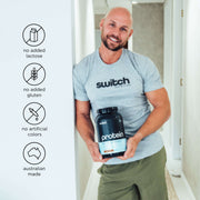 Smiling bald man wearing a Switch Nutrition t-shirt, holding a protein container with icons indicating no added lactose, gluten, artificial colors, and Australian made.