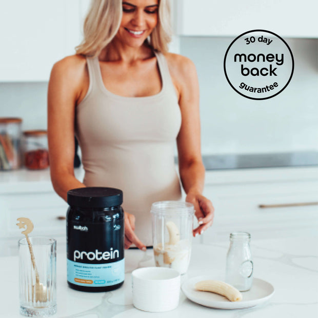 Woman in a beige tank top preparing a smoothie with Switch Nutrition Protein, bananas, and a milk bottle, with a &