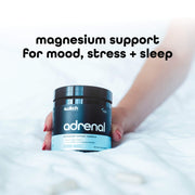 An image showing a person lying down holding a container of Switch Nutrition's 'adrenal' magnesium support formula for mood, stress, and sleep, against a white bedding background.