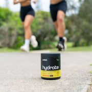Container of Switch Nutrition Hydrate on the ground with a person running in the background, emphasizing an active lifestyle.
