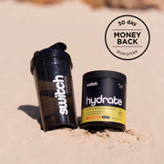 Switch Nutrition Hydrate container next to a water bottle on sandy beach, with a '30 day money-back guarantee' seal.