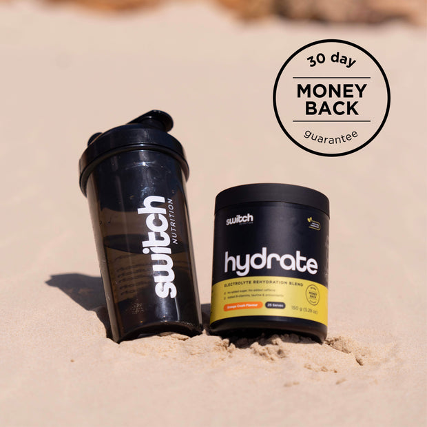 Switch Nutrition Hydrate container next to a water bottle on sandy beach, with a &