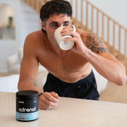 A male leaning on the kitchen bench drinking a hot cup of Adrenal Switch chocolate before bed.