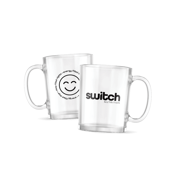 Two clear glass mugs from Switch Nutrition. One mug features the "Switch Nutrition" logo in black, while the other displays a smiling face graphic surrounded by the text "Energy Filled Days • Sleep Filled Nights" in a circular design. Each mug has a sturdy handle and a sleek, modern design.