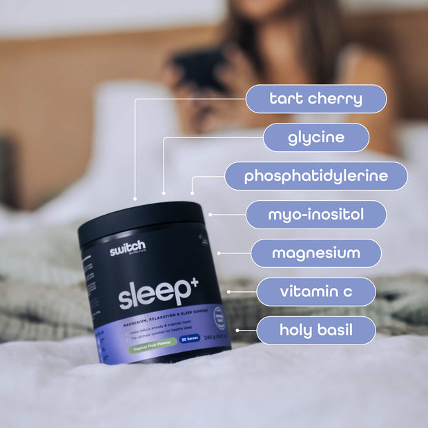 Sleep+ supplement container with labels highlighting key ingredients such as tart cherry, glycine, phosphatidylserine, myo-inositol, magnesium, vitamin C, and holy basil, with a blurred background of a person in bed.