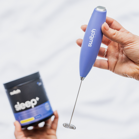 Person holding a purple Switch Nutrition Whiz Stick electric mixer, with a container of Sleep+ supplement in the background.