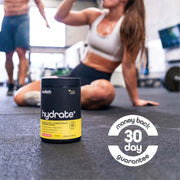  container of 'HYDRATE+' by Switch Nutrition is prominently displayed on the floor of a busy gym, with an athlete in the background in a yoga pose, which focuses on the lifestyle of active fitness enthusiasts. Emphasised at the bottom of the image is a 'money back 30-day guarantee', suggesting confidence in the product's efficacy and a commitment to customer satisfaction.