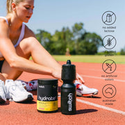 An athlete is seated on a running track, lacing her shoes, with a container of 'HYDRATE+' by Switch Nutrition and a matching sports water bottle beside her. To the right, icons indicate the product's attributes: no added lactose, no added gluten, no artificial colors, and it's Australian made. This setup emphasises the product's health-conscious and local production qualities within a sports and fitness context.
