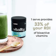 A green smoothie next to a container of Vitality Switch Greens Powder on a white background, with text highlighting that '1 serve provides 33% of your RDI of bioactive vitamins.