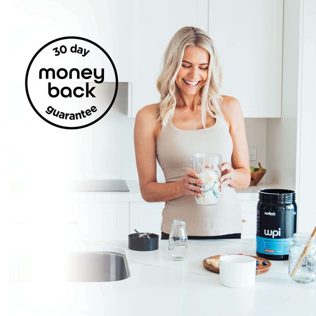 A smiling woman in a bright kitchen preparing a shake with Whey Protein Isolate (WPI), with a &